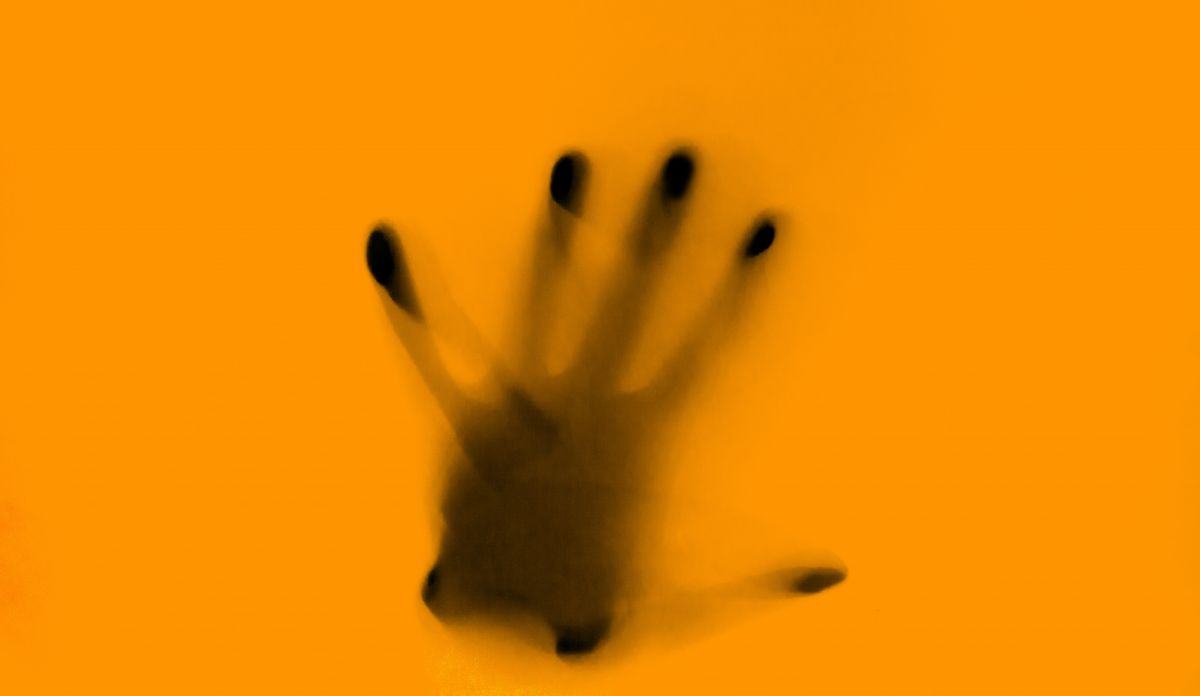 Photographie d'une main derrière une vitre jaune