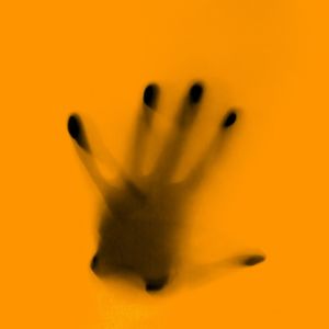 Photographie d'une main derrière une vitre jaune