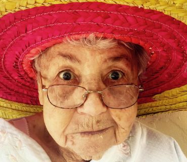 Photographie d'une vieille dame à lunettes avec un sombrero rouge et jaune